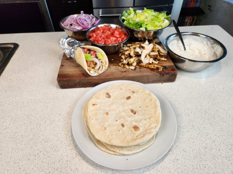 Grilled chicken with fresh pita plated on a counter top with veggies.